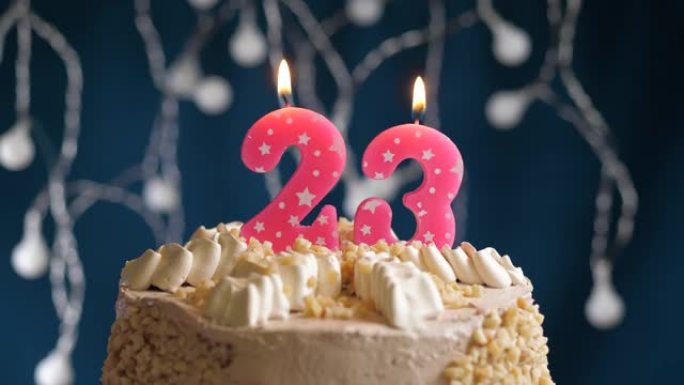 蓝色背景上有23号粉色蜡烛的生日蛋糕。蜡烛吹灭了。慢动作和特写视图