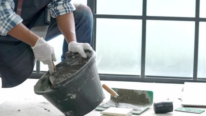 4k高级杂工手使用抹刀在桶中搅拌混凝土水泥砂浆，用于准备家庭装修维修施工或瓷砖铺路。高级男子diy工