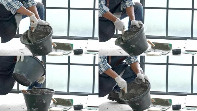 4k高级杂工手使用抹刀在桶中搅拌混凝土水泥砂浆，用于准备家庭装修维修施工或瓷砖铺路。高级男子diy工