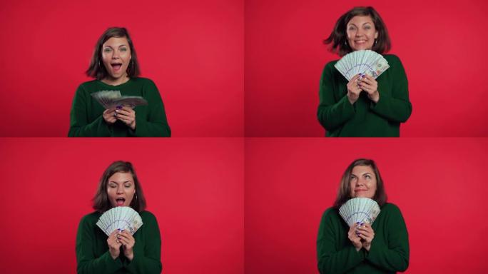 快乐兴奋的女孩穿着绿色毛衣显示钱-红墙上的美元钞票。成功、收获、胜利的象征。