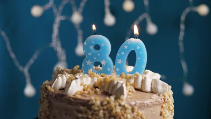 蓝色背景上有80号蜡烛的生日蛋糕。蜡烛着火了。慢动作和特写视图