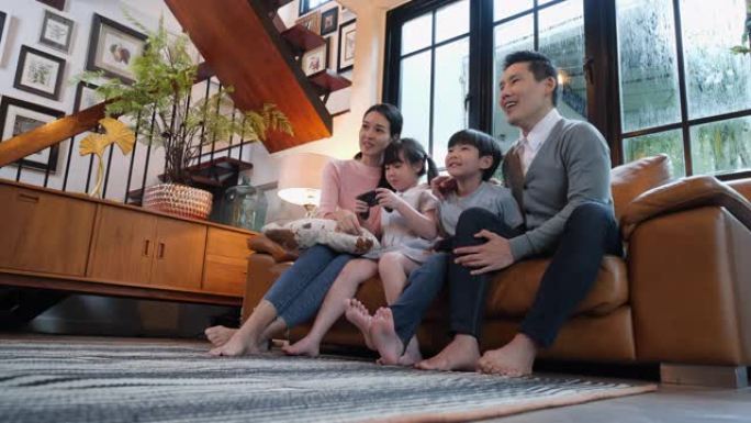 亚洲家庭周年快乐。活跃的父母和可爱的孩子儿子和女儿在现代房子的客厅玩电子游戏。玩得开心的男孩和女孩在