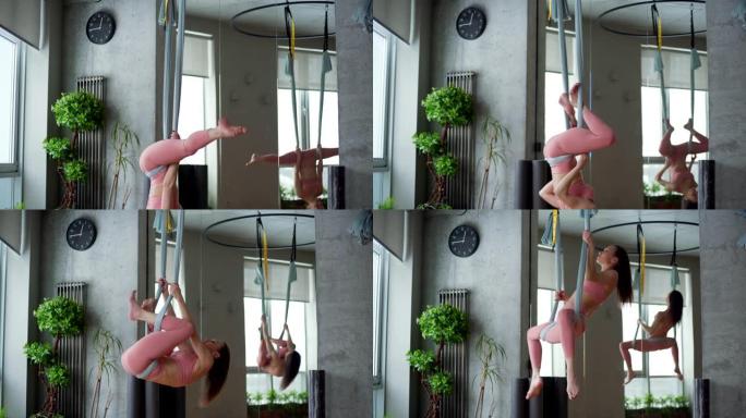 灵活而熟练的年轻女子在瑜伽馆的吊床上做空中瑜伽练习，墙上挂着大镜子