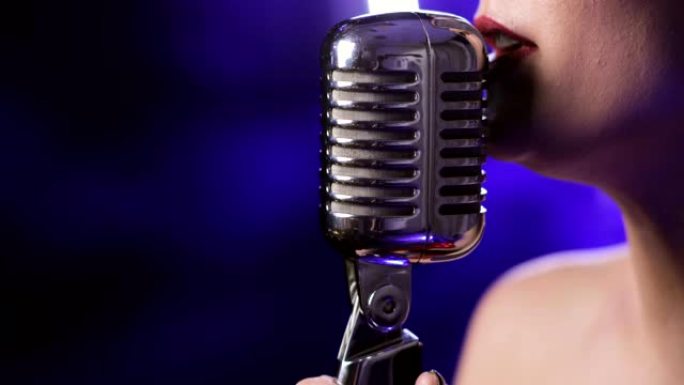 女歌手在蓝色背景上的麦克风上唱歌，特写嘴唇侧视图