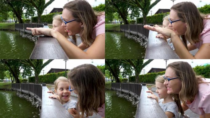 幸福的母女在城市公园的池塘上看
