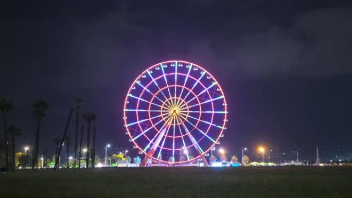 摩天轮在夜间旋转，带有彩色灯光