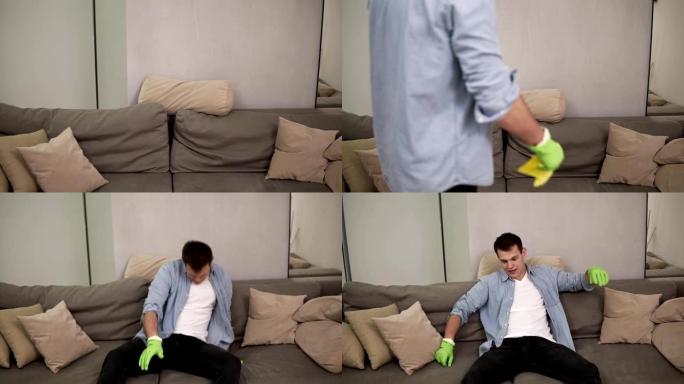 虚弱的年轻英俊男子打扫后倒在沙发上，洗木地板后感到疲倦。呼气。戴着绿色橡胶手套。慢动作