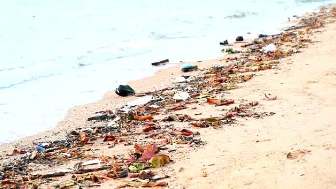 海滩上的日落用塑料橡胶和废物留在海滩上，海浪把它们吹入海边