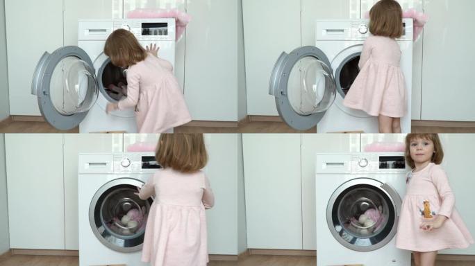 小微笑可爱的3岁女孩的肖像放入洗衣机玩具进行洗涤，关闭舱门并打开家用电器。儿童洗涤玩具