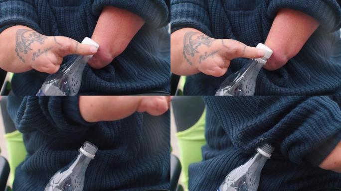 一个没有手的残疾人打开塑料瓶的盖子。