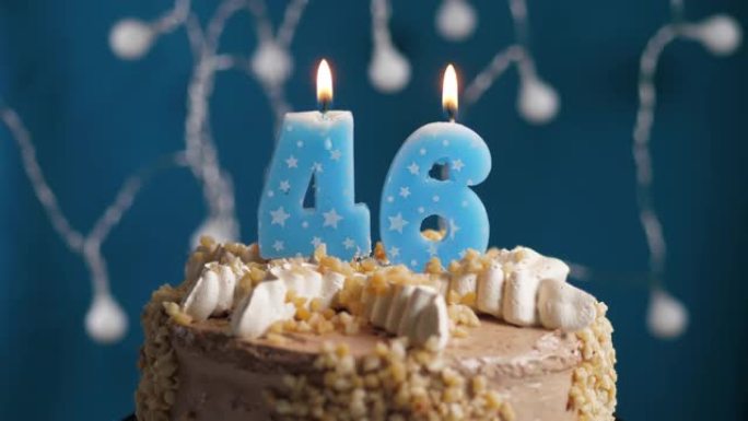 蓝色背景上有46号蜡烛的生日蛋糕。蜡烛吹灭了。慢动作和特写视图