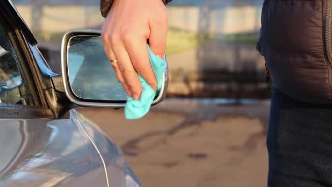 一名使用超细纤维的男子在汽车上擦拭后视镜。汽车护理概念。