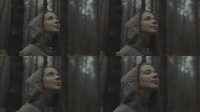 美丽的女人站在森林里，感到幸福。好看的女孩仰望天空，享受生活。时髦的少女旅行者在辛苦的一天工作后走到