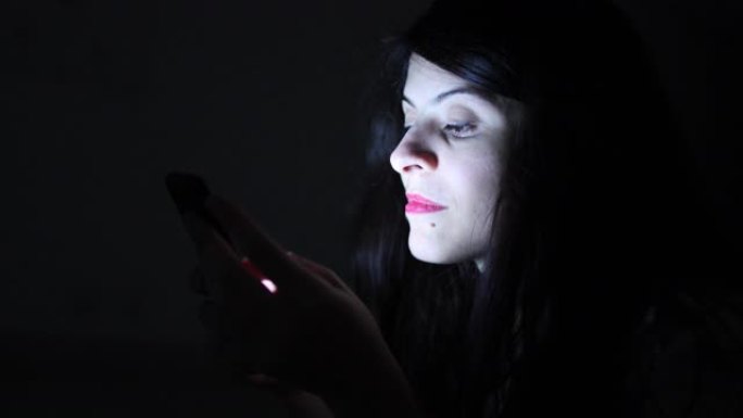 女人独自在黑暗中晚上使用智能手机设备