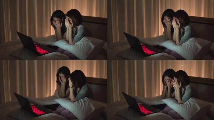侧视图: 两个年轻的女性朋友在晚上通过看笔记本的恐怖系列在床上一起分享片刻