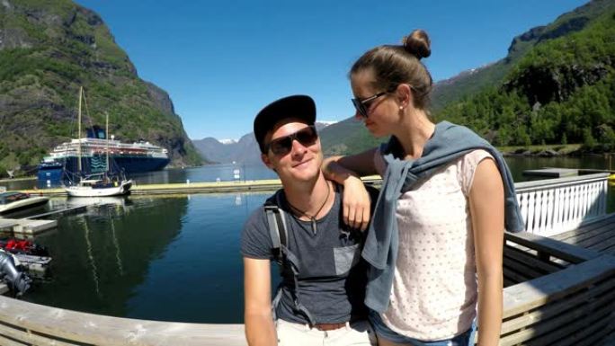 一对夫妇坐在挪威一个小港口的鞋子上。他们互相看着，玩得很开心。爱和同情。他们被高大的山脉包围着。探索