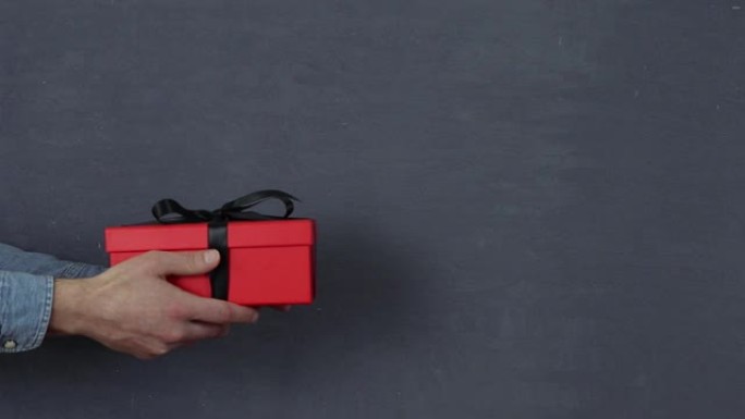 一只手在木制桌子上放一个带有黑色丝带的红色礼品盒，孤立的背景。情人节快乐