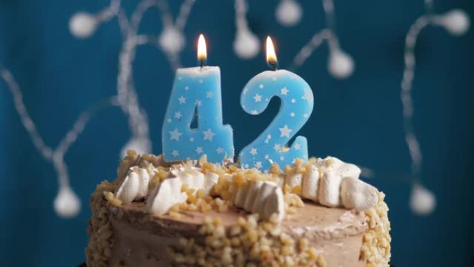 蓝色背景上有42号蜡烛的生日蛋糕。蜡烛吹灭了。慢动作和特写视图