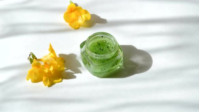 玻璃罐与天然绿色猕猴桃果实磨砂膏和黄色小苍兰花。