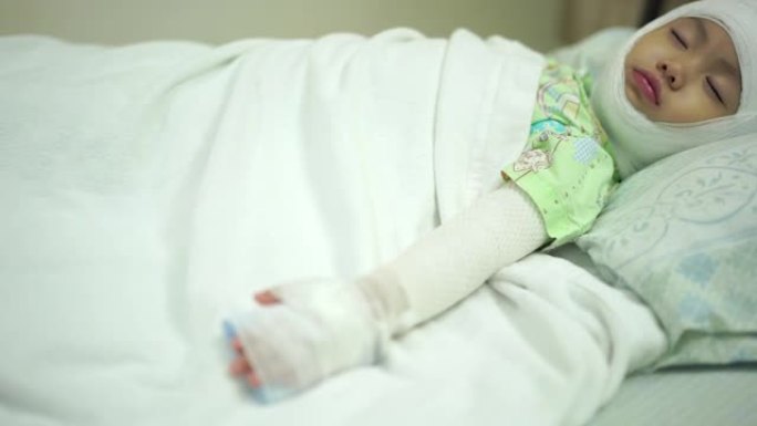 亚洲女婴躺在医院，头部和手臂被绷带包扎在床上。头部和手臂受伤的女婴。手持镜头，真实生活
