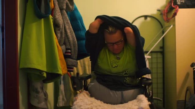 一个残疾人在公寓的走廊上脱下毛衣。