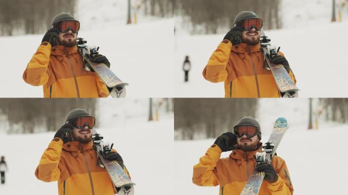 一个人拿着滑雪板打电话。背景是滑雪坡和雪山。股票视频