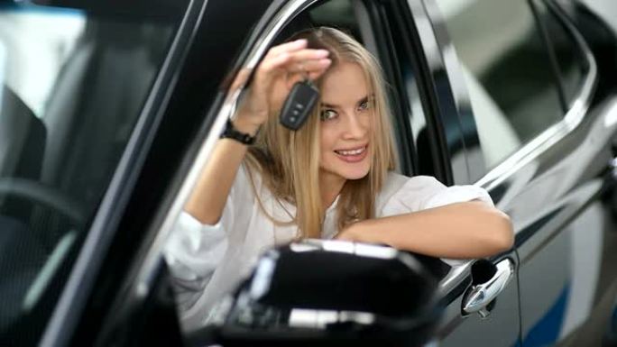 快乐的女人买了一辆新车。她正坐在方向盘上微笑着拿着钥匙