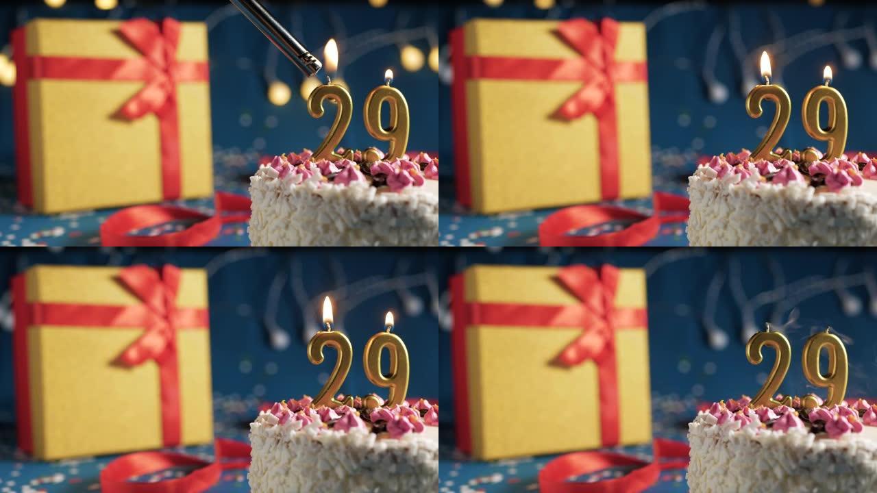 白色生日蛋糕29号点火器燃烧的金色蜡烛，蓝色背景带灯和用红丝带绑起来的礼物黄色盒子。特写