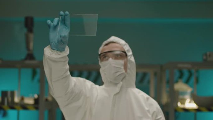 专业医生生物化学家拿着和看方形玻璃。现代实验室中穿着白色防护服的男科学家肖像。男子研究员手里拿着玻璃
