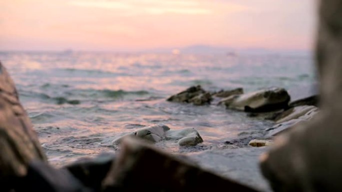 特写慢动作低角度小海浪在岩石海滩上滚动。海边。鹅卵石岩石海滩上的日落