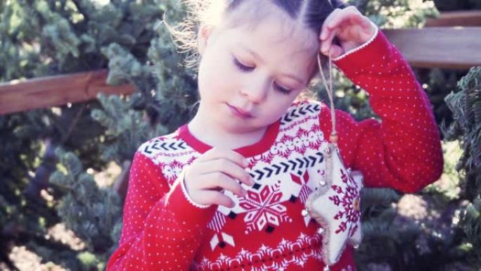 穿着红色连衣裙的小女孩在圣诞树农场拿着圣诞装饰品。
