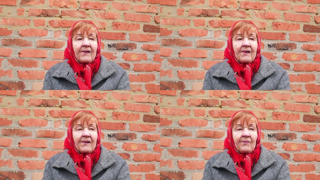 穿着红围巾的老妇在砖墙背景上。母亲节。祖母。人。年龄。面部表情。