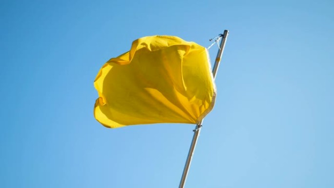 在蓝天的映衬下，海滩上随风飘扬的黄旗。缓慢的运动。高清