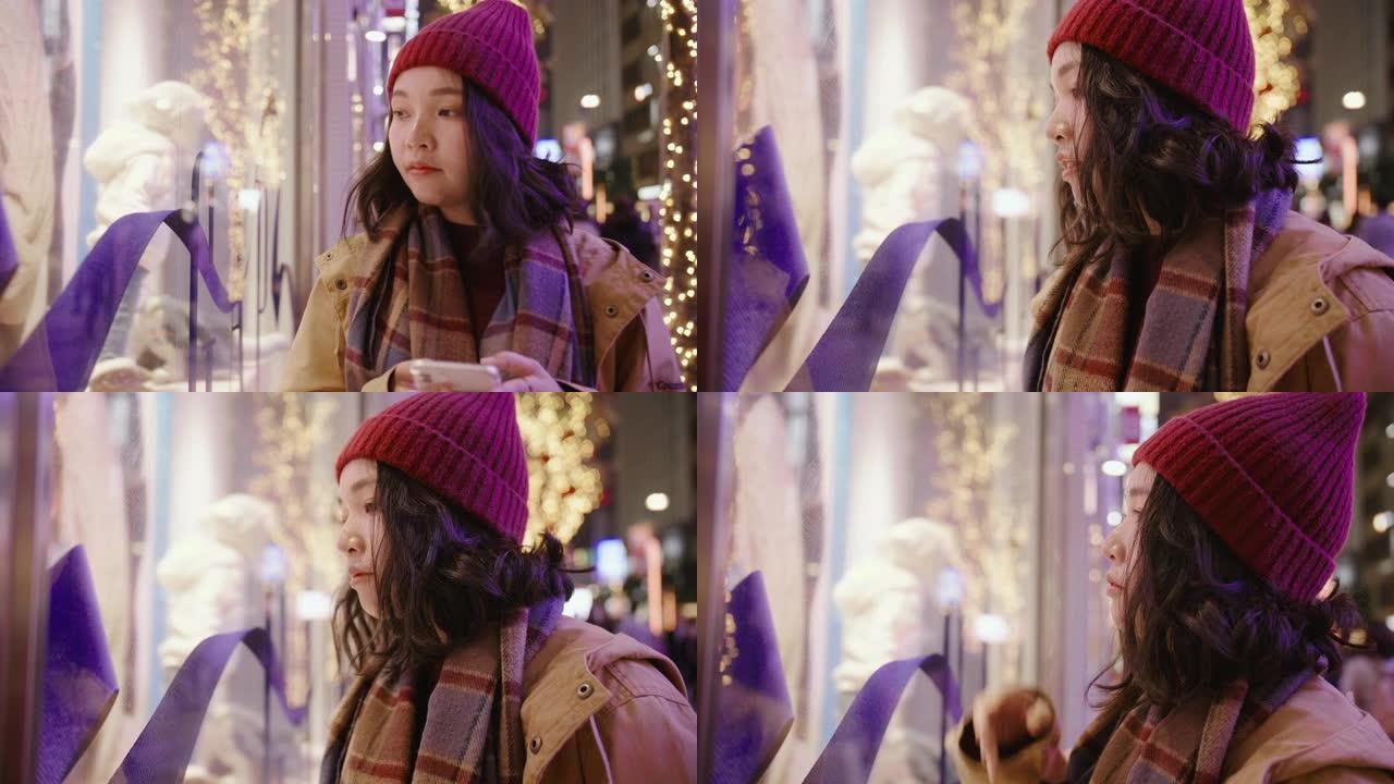 亚洲女孩戴上羊毛帽子和围巾。她在城市的圣诞市场购物。