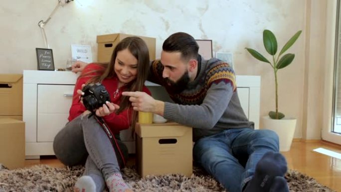 年轻夫妇坐在新家的地板上看着相机上的照片
