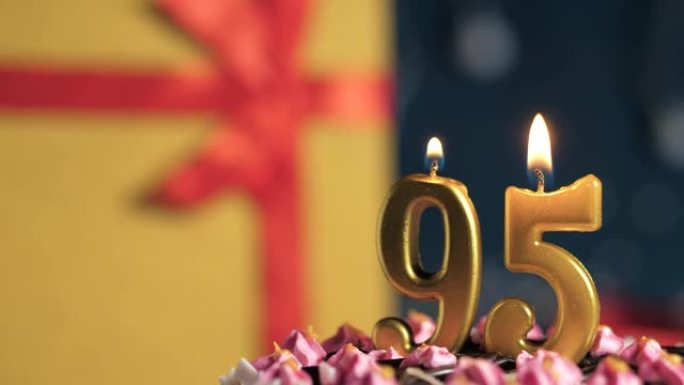 生日蛋糕95号点火器燃烧的金色蜡烛，蓝色背景礼物黄色盒子用红丝带绑起来。特写和慢动作