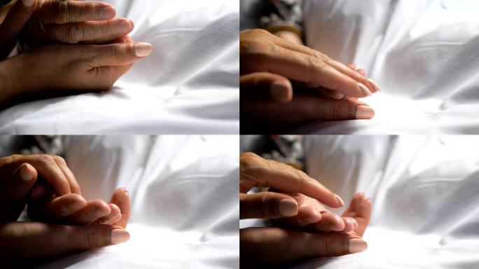 无法辨认的女人握住并轻轻地抚摸母亲的手，表现出关怀或爱心。女儿安慰躺在诊所床上的年迈妈妈的皱纹手臂。