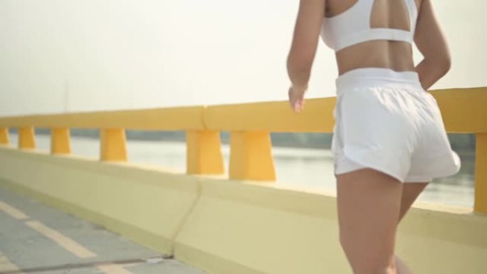 慢动作运动员女子在海滩路上跑步。亚洲女跑者夏季耐力训练。健康的生活方式和运动