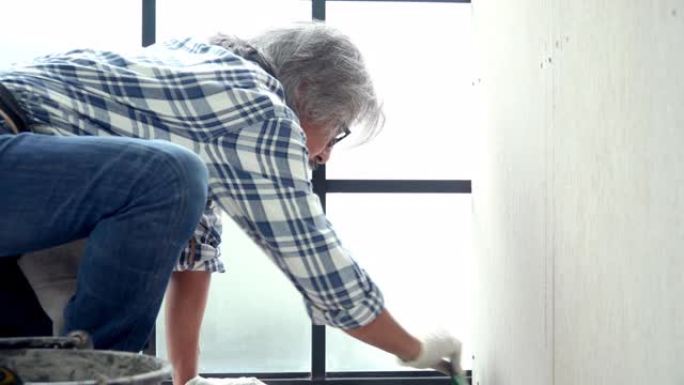 4k亚洲高级杂工用抹子用水泥铺砖地板。高级技术员修理建筑工程或瓷砖房间地板的家庭装修。资深老人diy