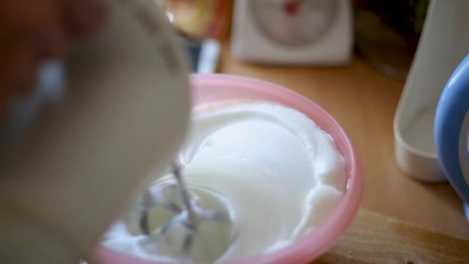 用手动搅拌器在不锈钢碗中混合或搅拌鸡蛋，用蓬松的白色蛋白酥皮和橙色蛋黄