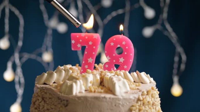 蓝色背景上有79号粉色蜡烛的生日蛋糕。蜡烛着火了。慢动作和特写视图