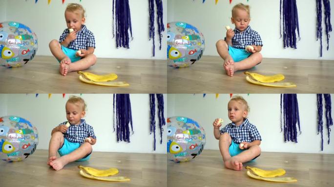 可爱的小孩坐在地板上吃香蕉。手里拿着香蕉的帅哥