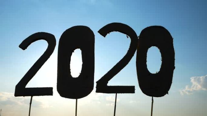 回收纸板的剪影变成2020的数字，在蓝天背景和阳光照耀着文本。新年和庆祝活动的概念。