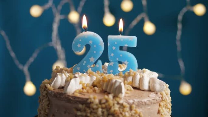 蓝色背景上有25号蜡烛的生日蛋糕。蜡烛吹灭了。慢动作和特写视图