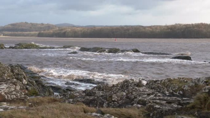 在苏格兰一个刮风的早晨，从岸上看淤泥海水冲刷在岩石上。