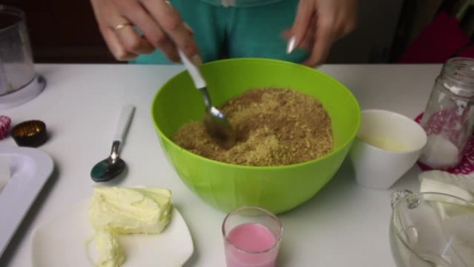 一个女人在碎饼干中添加可可和黄油。其他制作土豆饼干的配料也在附近摆放。