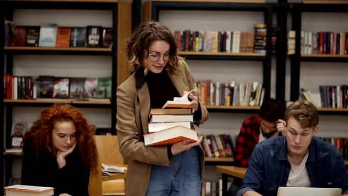 一个穿着棕色夹克和眼镜的女孩的慢动作镜头，她从书架上拿了一堆书，开始看书。其他学生坐着，在大学、大学