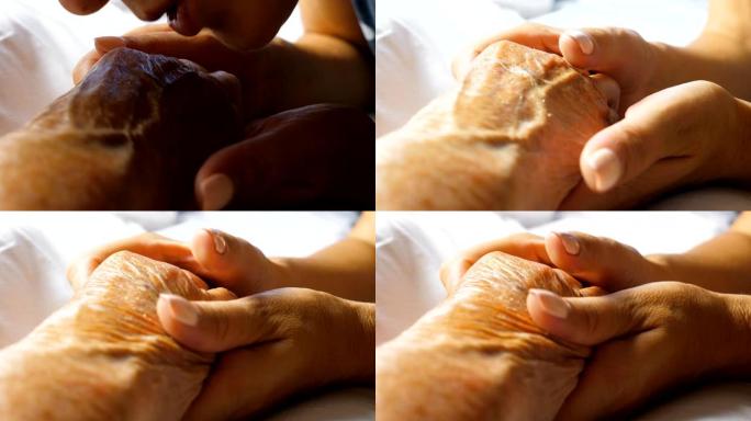 无法辨认的女人轻轻地抚摸着母亲的手，亲吻着母亲的手，表现出关怀或爱。女儿安慰躺在床上的年迈妈妈皱巴巴