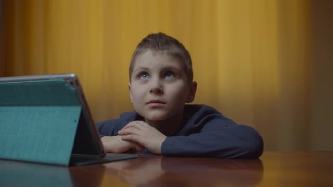 自闭症男孩的肖像使用平板电脑坐在办公桌前。家里有小玩意的自闭症孩子。自闭症意识