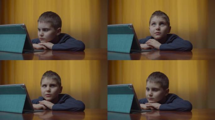 自闭症男孩的肖像使用平板电脑坐在办公桌前。家里有小玩意的自闭症孩子。自闭症意识